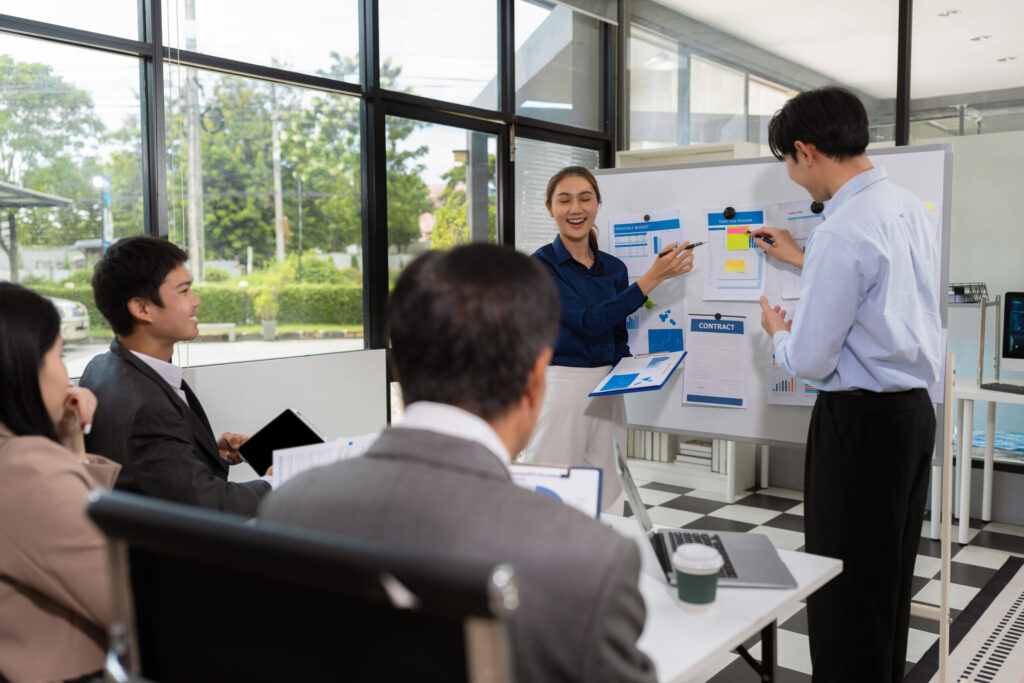 A sales enablement lead running a workshop at a whiteboard with a team of sellers